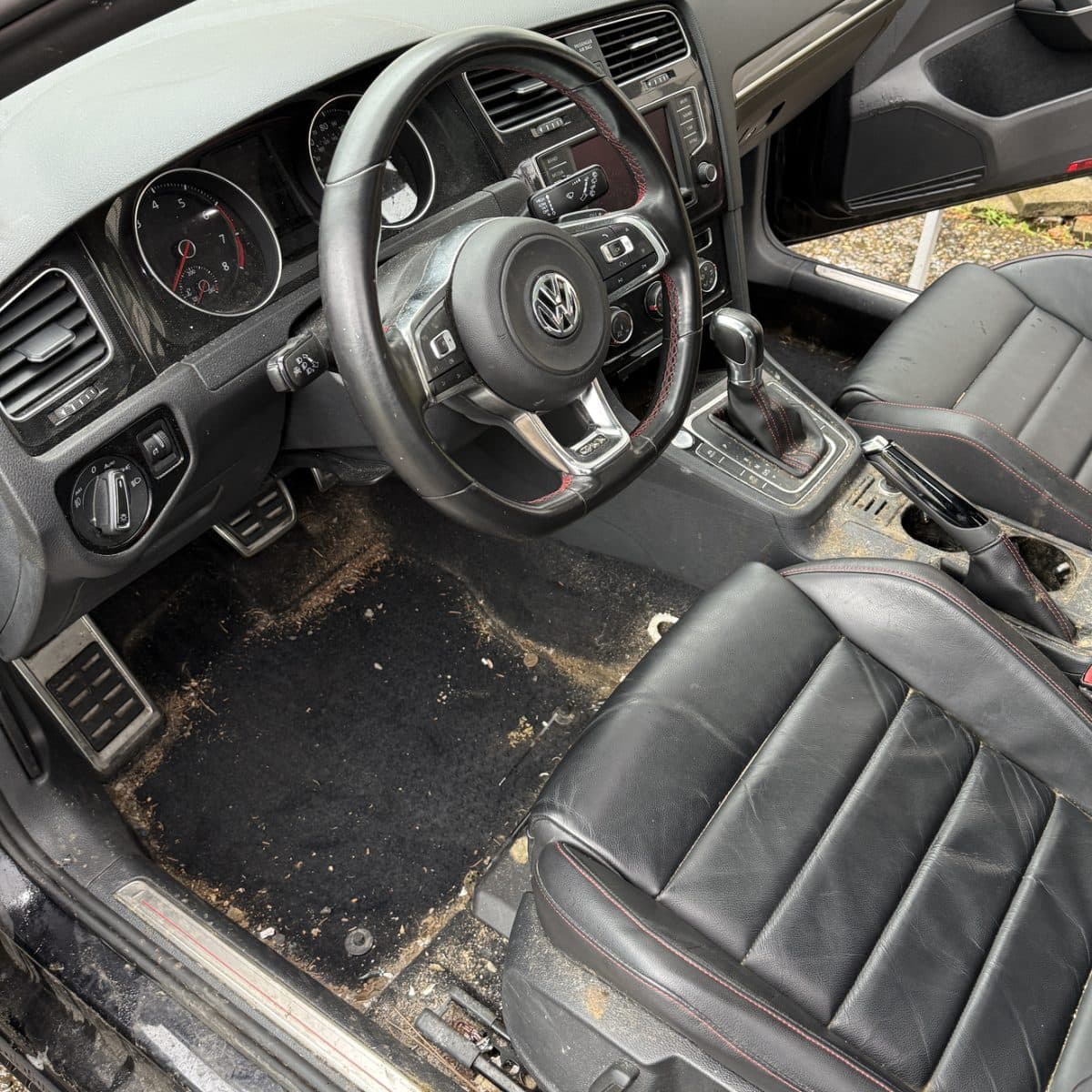 Volkswagen GTI interior before detailing, with dirt and debris covering the driver's floor