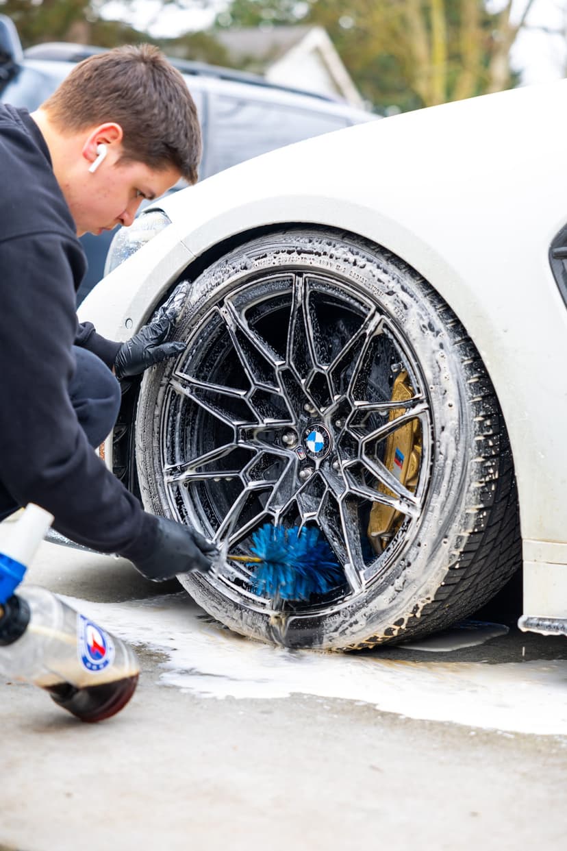 Detailer scrubbing a BMW wheel with a brush during a mobile wash