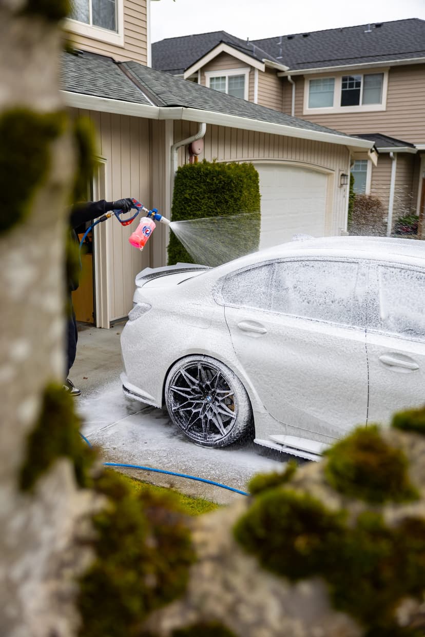 Detailer foaming a white sedan in a driveway during a mobile hand wash
